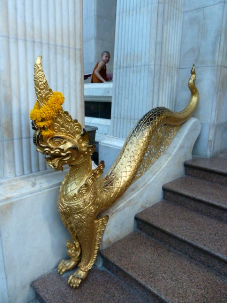 A novice Buddhist monk and a dragon guard the entrance to Wat Bowoniwes in Banglamphu, Bangkok, Thailand.