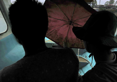 A tourist couple busts open an umbrella on the ferry back to Panajachel, Lago de Atitlan, Guatemala.