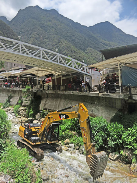 A backhoe goes to town moving rocks in the river at Aguas Calientes, Peru.