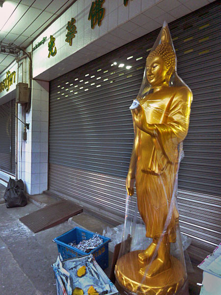 Plastic Buddha meets plastic shrinkwrap in Bangkok, Thailand.