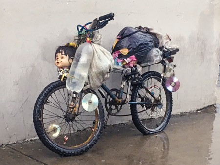 A funky bicycle adorned with an old doll's head, CD-Rs, bags, bottles and who knows what else in Leon, Nicaragua.